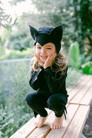 Child wearing a black cat Halloween costume while sitting on a wooden bench outdoors