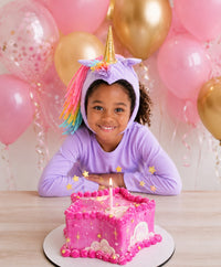 Child wearing a lavender unicorn costume with a golden horn and pastel rainbow mane