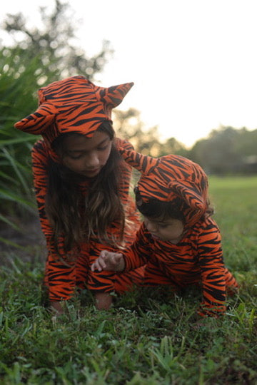 Two children wearing matching tiger costumes while playing outdoors
